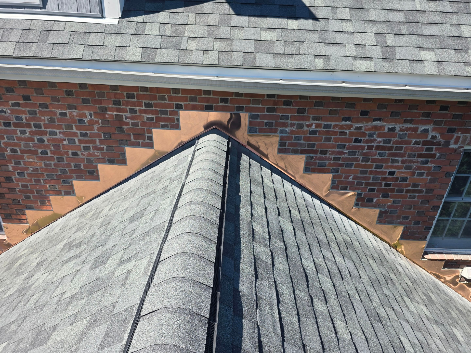 Custom copper step flashing where a shingle roof meets brickwork